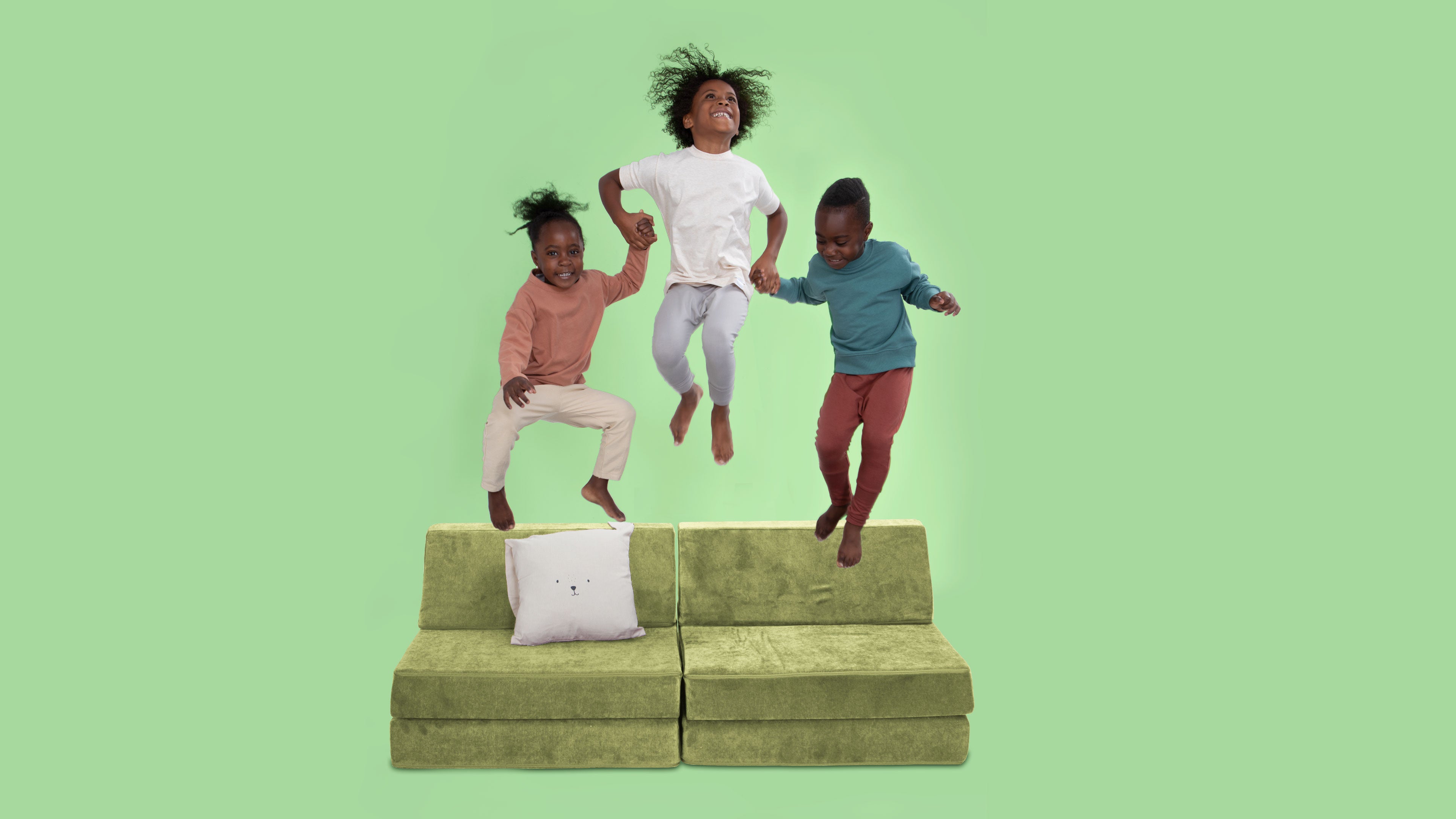 three kids jumping and laughing on a green play couch