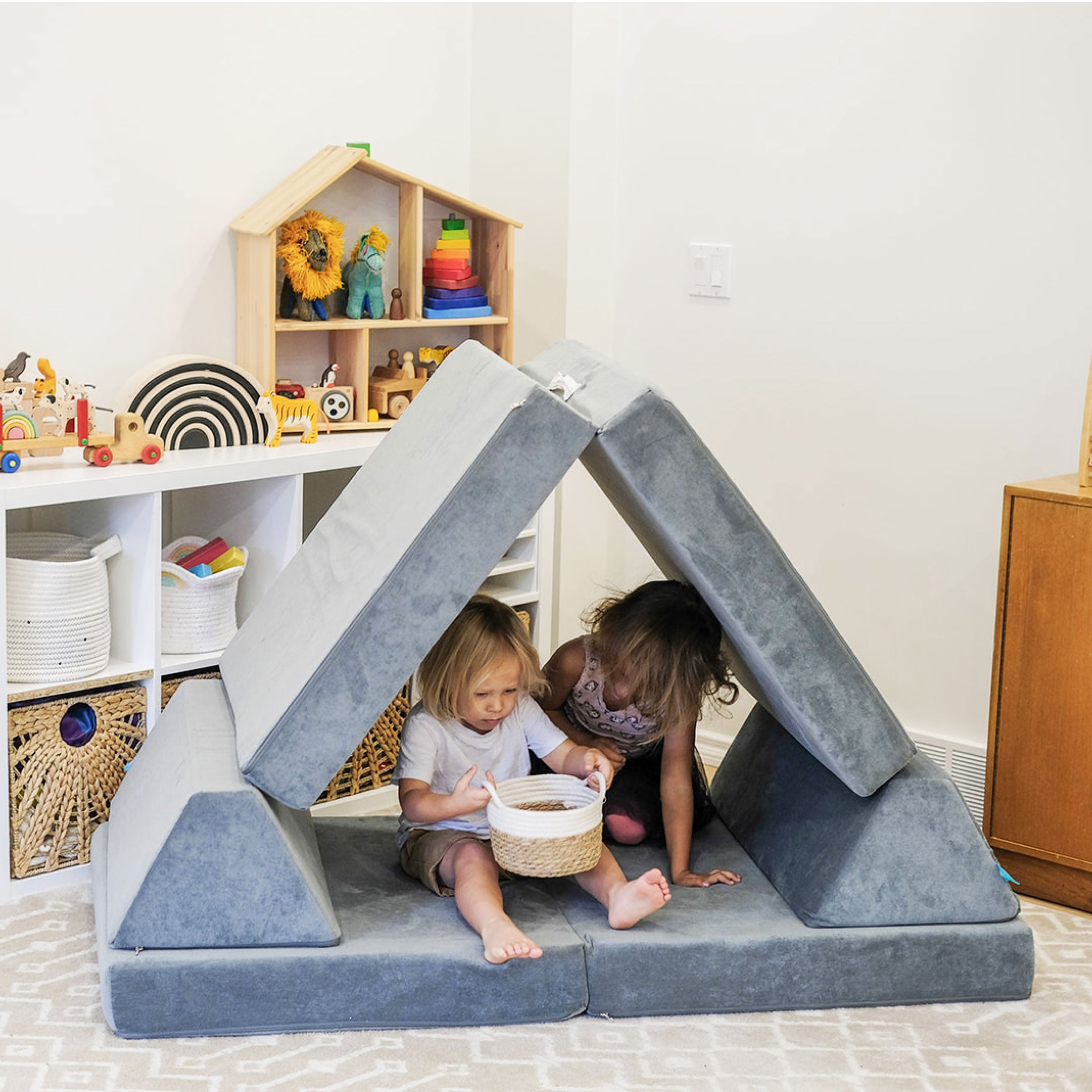 two kids looking at a basket with toys while inside a play couch in the shape of a house