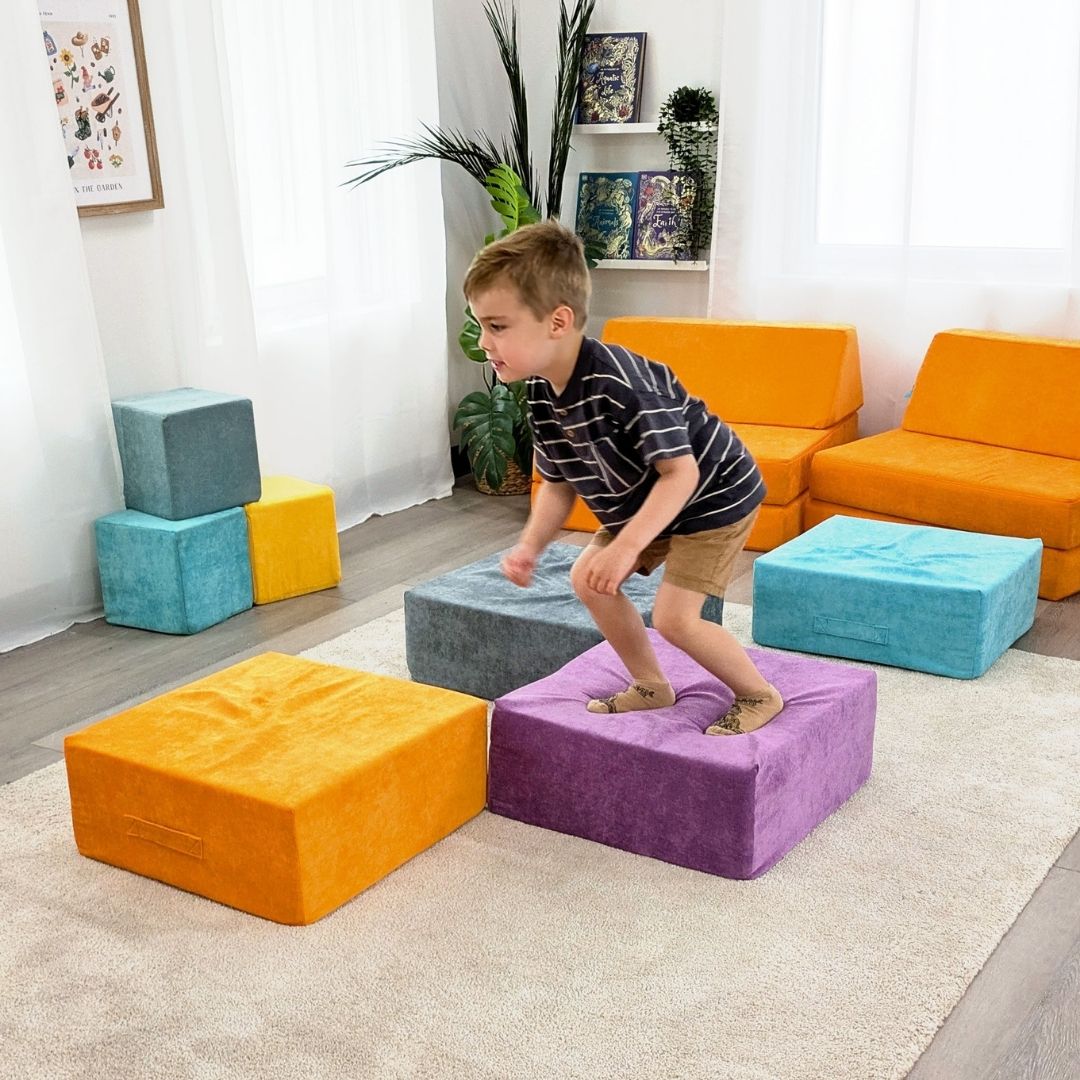 Child playing on colorful foam blocks in a room with orange couches and decorative plants.